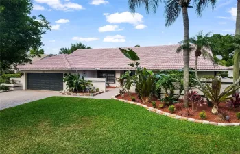 A beautifully paved driveway leads to an inviting front entrance, framed by lush, tropical landscaping and mature trees that provide both privacy and a touch of nature's tranquility.